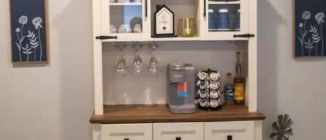 A kitchenette with a coffee bar sign, storage cabinets, a wine rack, and a pet bowl.