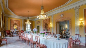 Une salle à manger élégante, avec une longue table dressée pour un repas, entourée de chaises richement décorées.