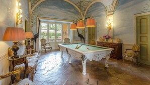 Une salle de billard équipée d’une table de billard, de fauteuils élégants et offrant, par une porte vitrée, une vue sur un espace extérieur.