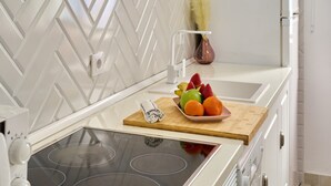 Uma cozinha com revestimento branco em padrão losango, tábua de corte de madeira com frutas e eletrodoméstico branco.