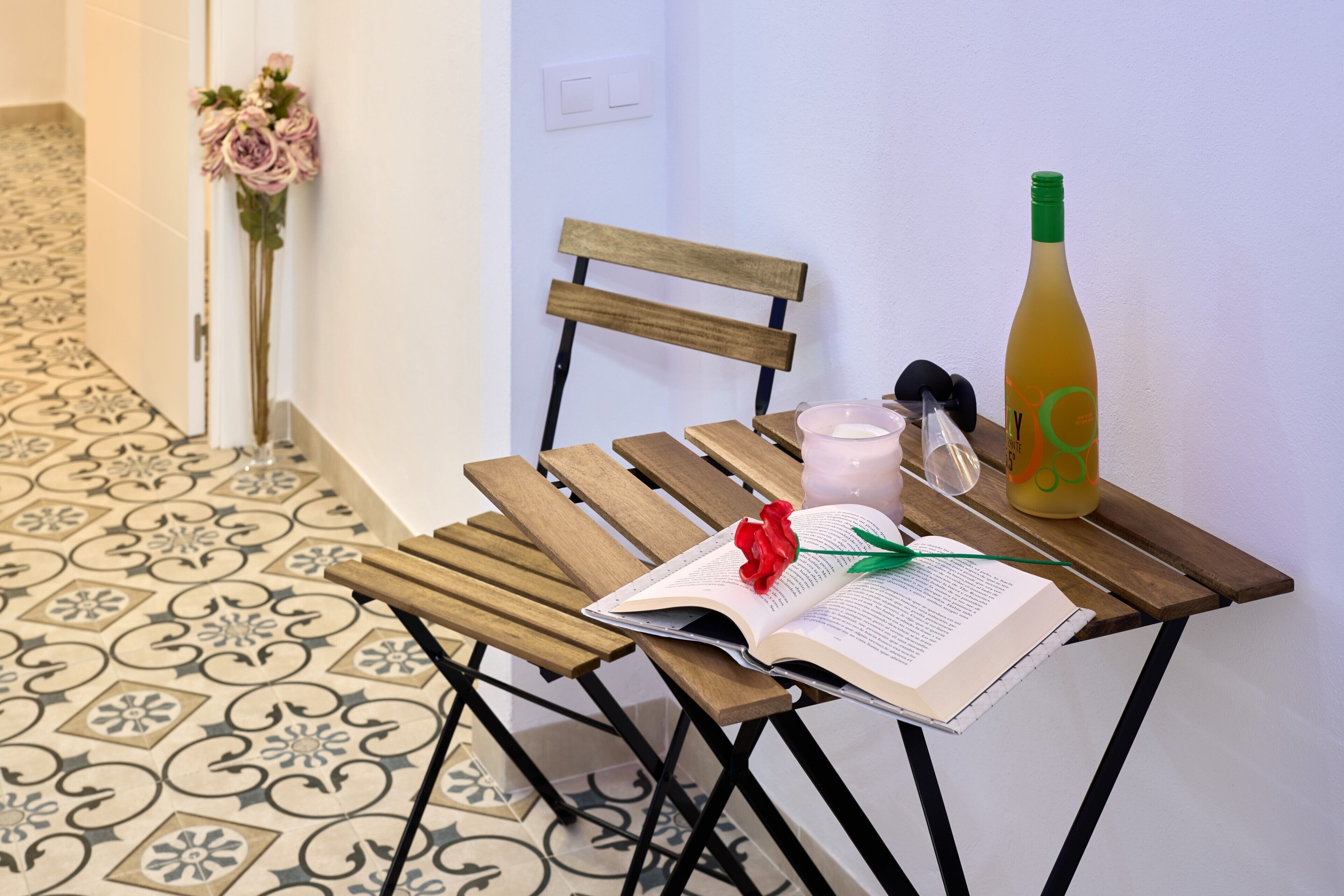 Una sedia di legno con un libro, una rosa, una bottiglia e un bicchiere su un tavolo.