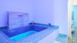 Um banheiro com banheira de azulejos, parede de pedra e piso revestido.