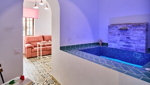 Um quarto com piscina azulejada, parede de pedra, sofá rosa e piso estampado.