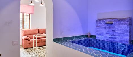A room with a tiled pool, a stone wall, a pink sofa, and a patterned floor.