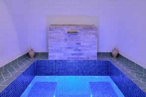Une piscine rectangulaire aux murs recouverts de carreaux bleus et un mur en pierre doté d’une ouverture de ventilation.