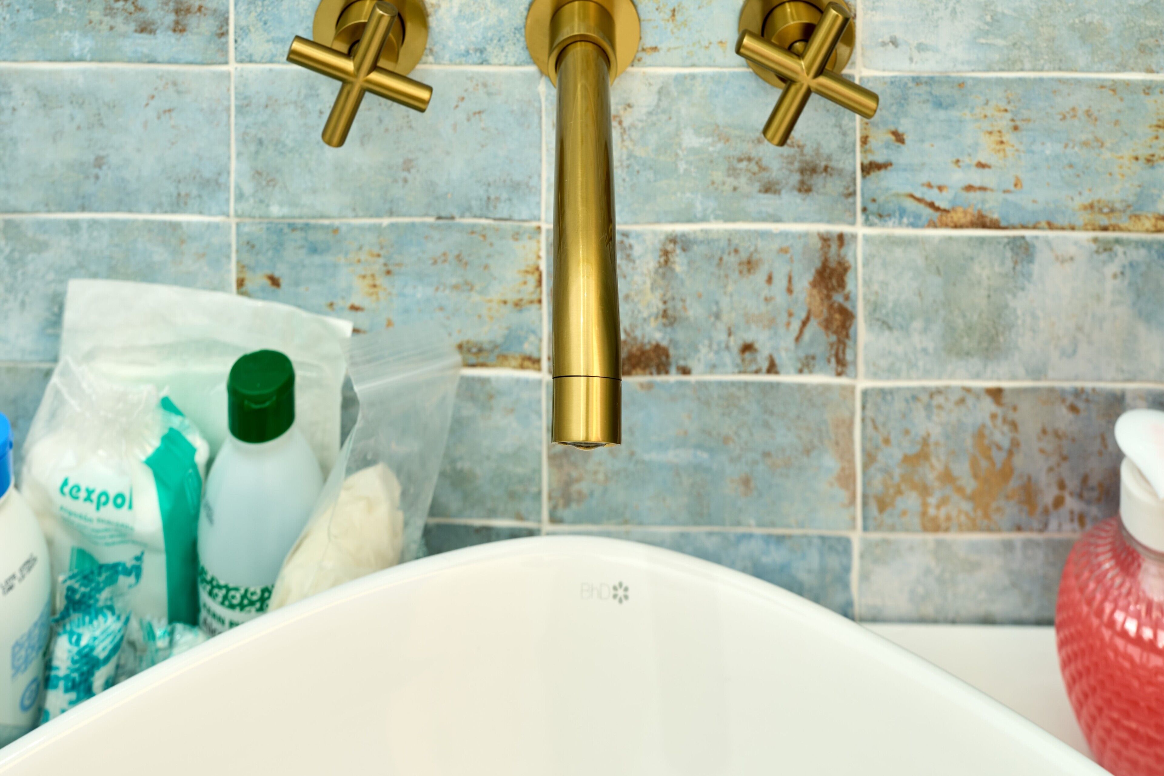 A bathroom with a white bathtub, a gold faucet, and a tiled wall.