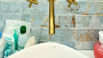 A bathroom with a white bathtub, a gold faucet, and a tiled wall.