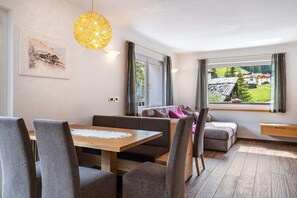 Een moderne kamer met een eettafel, zitplaatsen, een groot raam met uitzicht en een hanglamp.