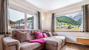 A modern living room with a sectional sofa, large windows, and a view of a mountainous landscape. - Apartment 'Mozart' with Mountain View, Balcony and Wi-Fi (Selva in Val Gardena)