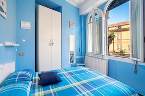 A bedroom with a bed, a wardrobe, a chair, and a window with a view of buildings.