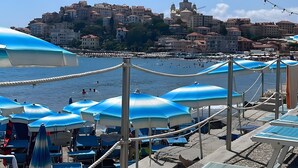 Une plage avec des parasols, des chaises longues et, au loin, une vue sur une ville historique.