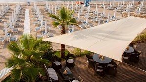 Un complexe hôtelier situé en bord de mer, doté de chaises longues, d’une tour de surveillance pour les sauveteurs et d’une terrasse avec des tables et des chaises.