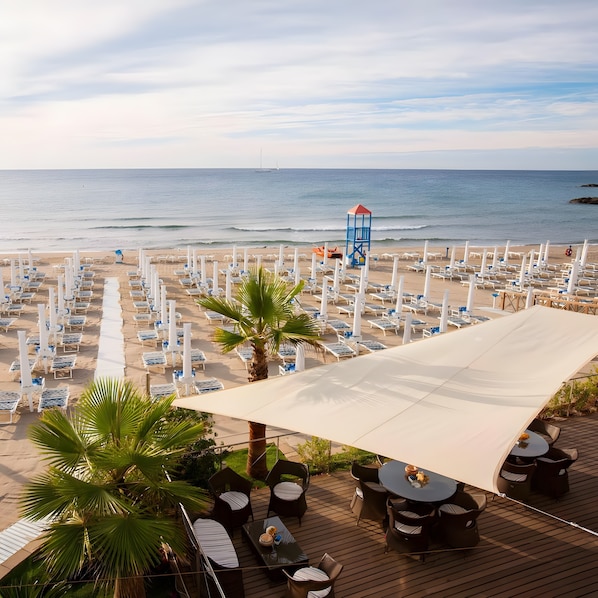 A beachside resort with sun loungers, a lifeguard tower, and a deck area with tables and chairs.