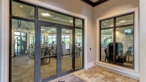 Entrada de gimnasio con puertas de vidrio, equipo de ejercicios en el interior y un felpudo con la inscripción 'EWG'.