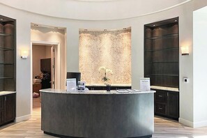 Un área de recepción con un mostrador central, un muro con diseño y armarios de madera oscura.