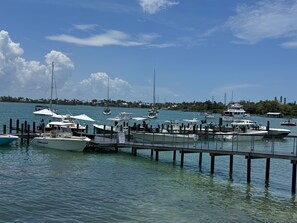 A marina with various boats docked, a pier extending into the water, and a distant shoreline with buildings.