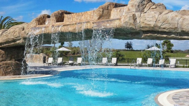 Una piscina con un arco de roca, agua azul cristalina y sillas de descanso.
