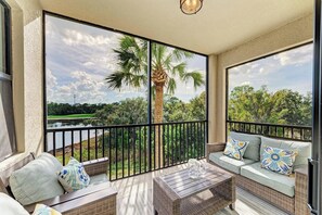 Un balcón con mobiliario de mimbre, vista a un lago y palmeras.