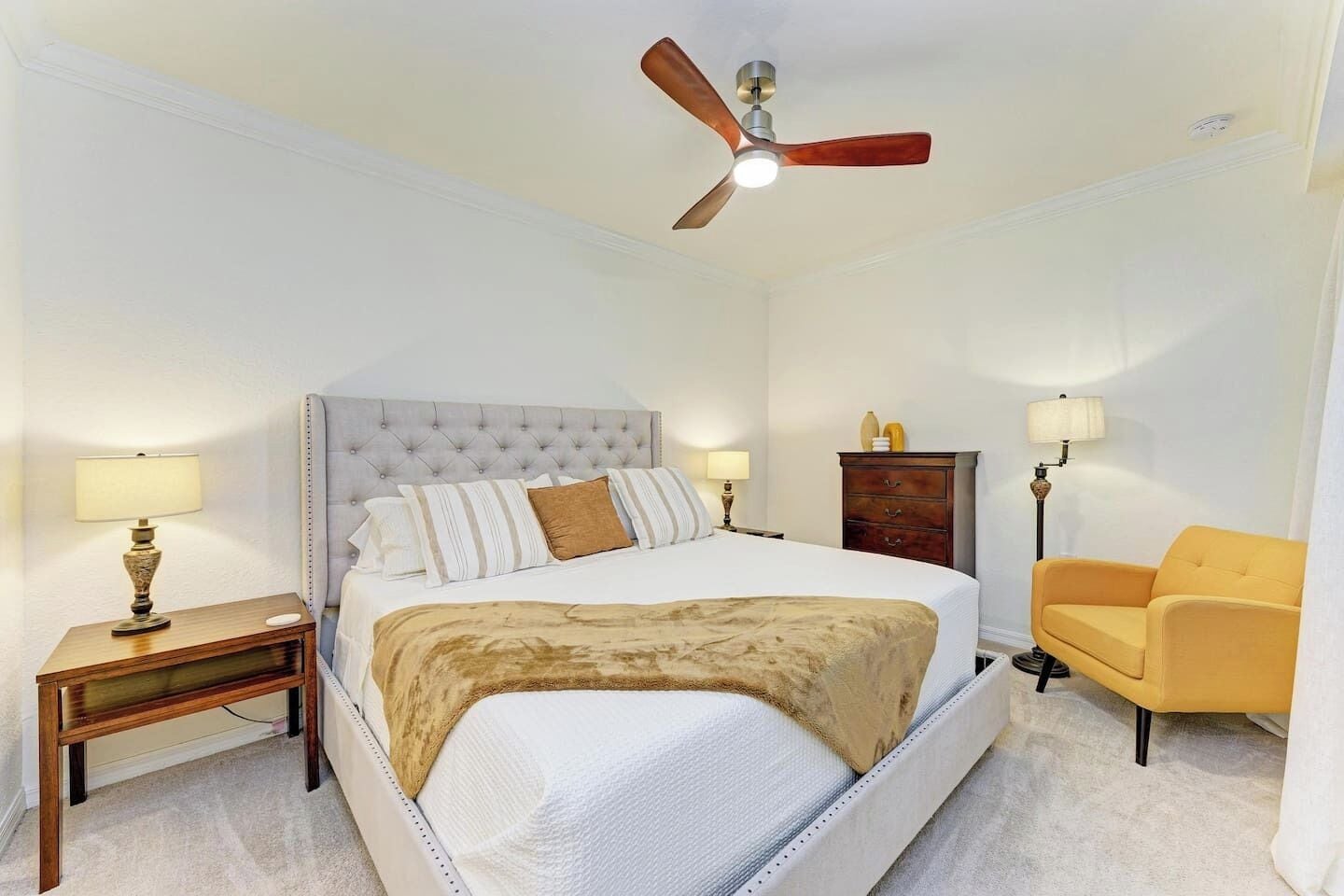 A bedroom with a bed, a nightstand, a dresser, a chair, and a ceiling fan.