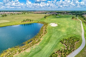 Ein Golfplatz mit Teich, einem Fußweg und weiter Aussicht auf ein Wohngebiet.