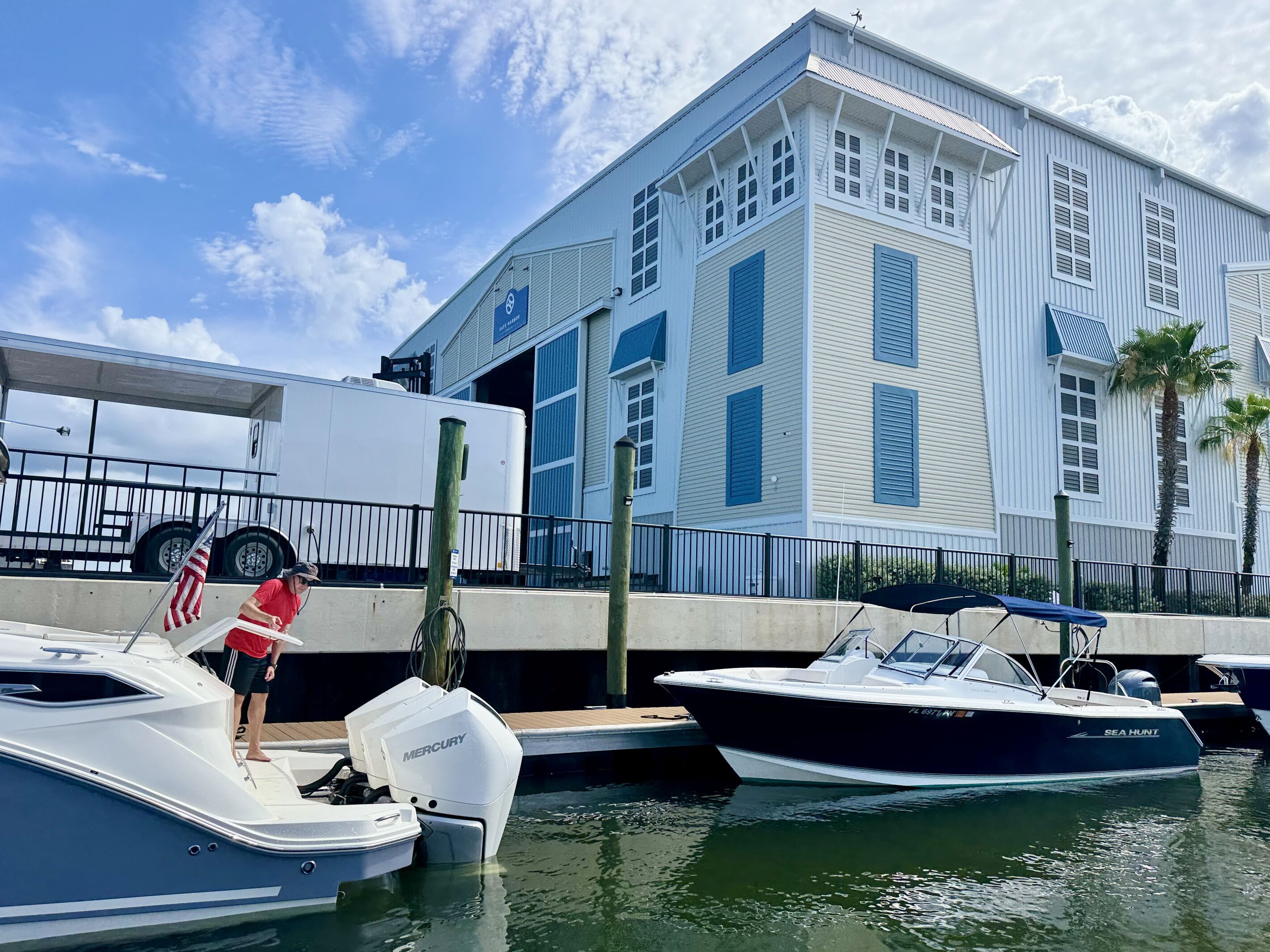 A marina with boats docked, a large building with multiple windows and shutters, and a person standing on a boat.