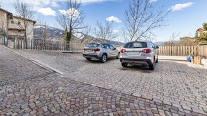Un estacionamiento pavimentado con dos coches aparcados, una valla de madera y montañas al fondo.