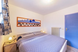 Quarto com cama, mesa de cabeceira, obra de arte na parede e porta azul.