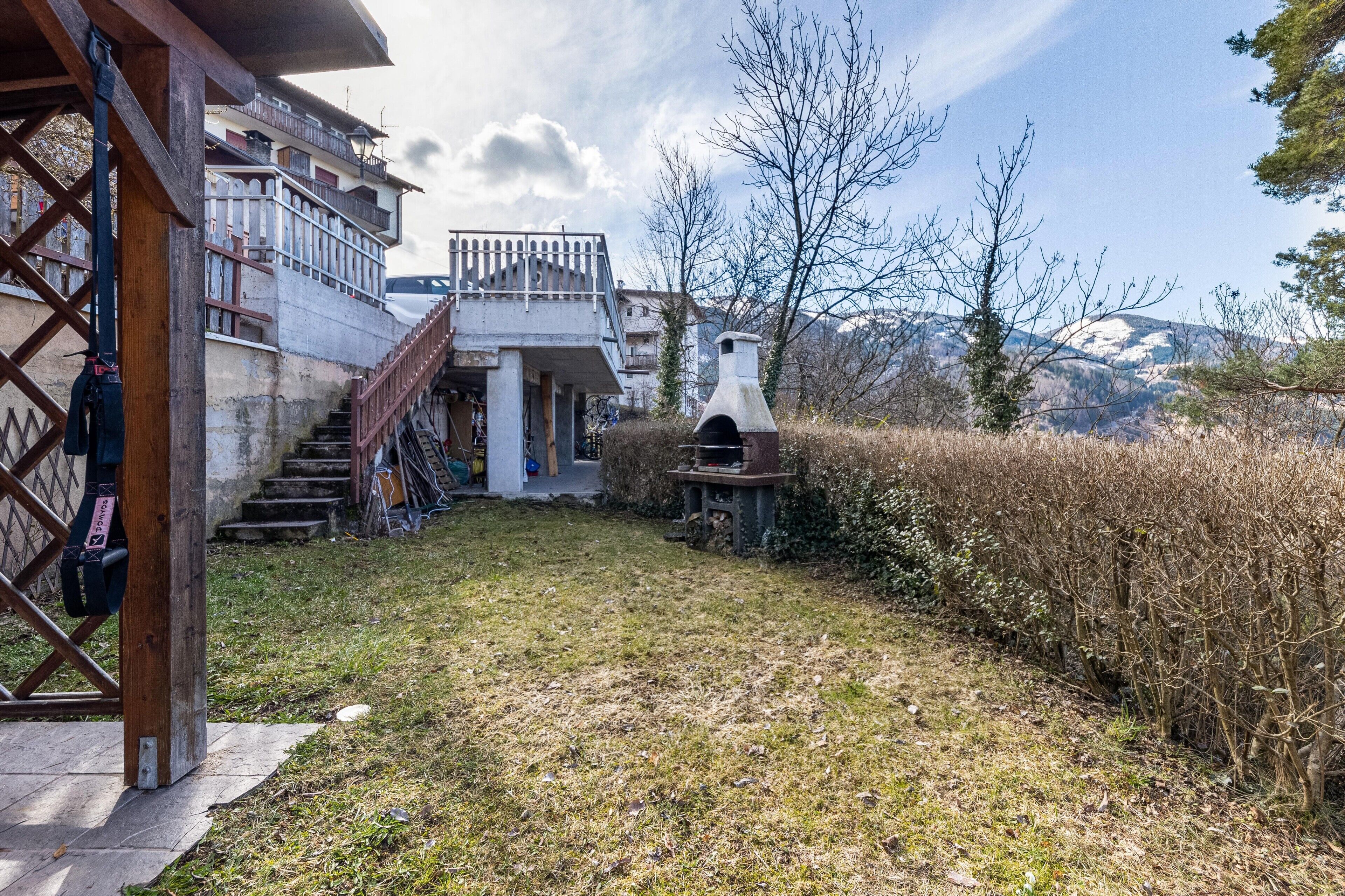 A residential building with a staircase leading to a balcony, a chimney, and a view of mountains.