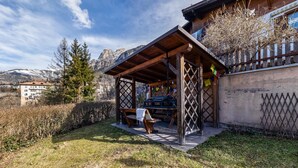 Un espacio de estar al aire libre con bancos y mesa, rodeado por una valla de madera y un telón de fondo de montañas.