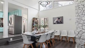A modern dining area with a black and white table, white chairs, and a stone accent wall. - Yosemite Lakehouse Sleeps 20 + Hot Tub + Game Room + BBQ (Oakhurst)