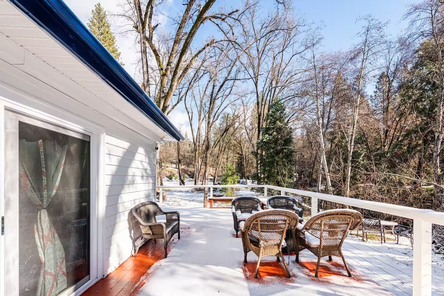 Une terrasse extérieure couverte, dotée de chaises en osier et d’un plancher en bois, et entourée d’arbres.