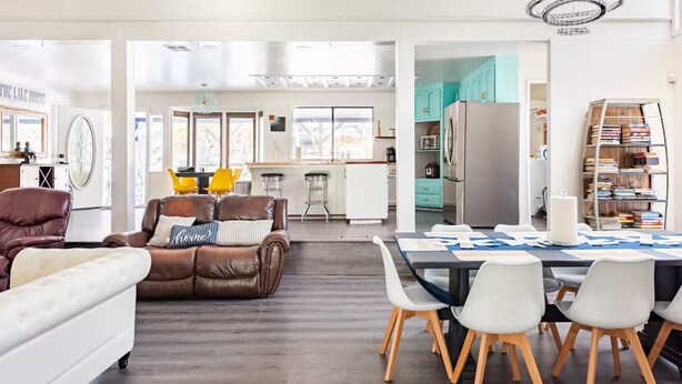 A spacious living area with a leather sofa, a dining table with chairs, and a kitchen in the background. - Yosemite Lakehouse Sleeps 20 + Hot Tub + Game Room + BBQ (Oakhurst)