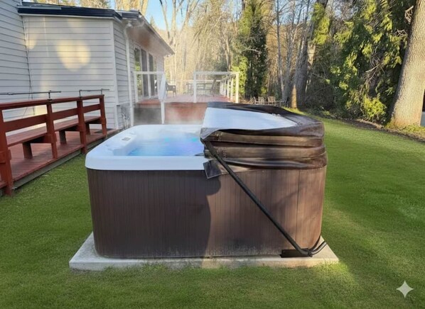 Un jacuzzi en un patio trasero con terraza de madera y una casa al fondo.