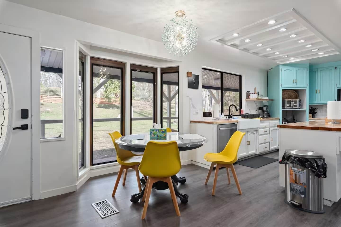 A modern kitchen with a dining area, large windows, and a view of the outdoors.