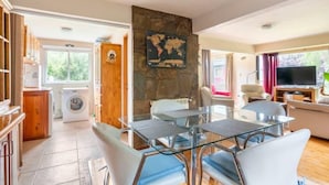 A modern living room with a glass dining table, comfortable seating, a flat-screen TV, and a stone fireplace.