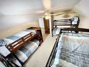 A dormitory room with two bunk beds, a ceiling fan, and a door leading to another room. - Hidden Bliss-Large 4 bedroom home at Mt Storm Lake (Mount Storm)