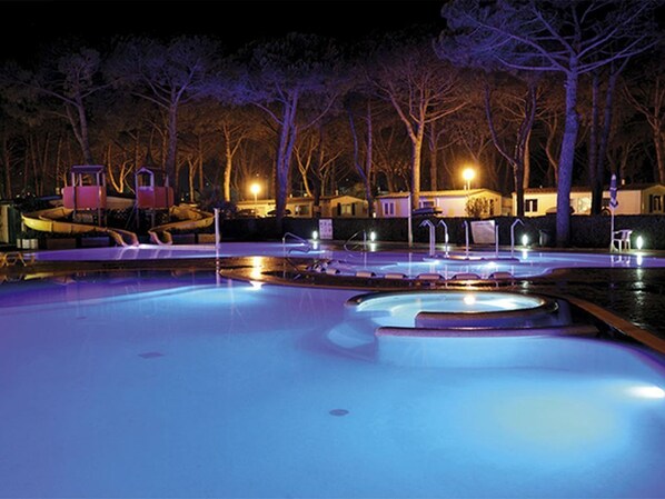 Zona de piscina nocturna con múltiples fuentes y luces iluminadas.