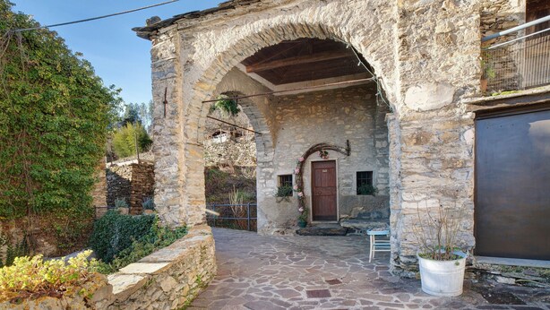 Un edificio de piedra con un arco de entrada, una puerta de madera y una planta en maceta.