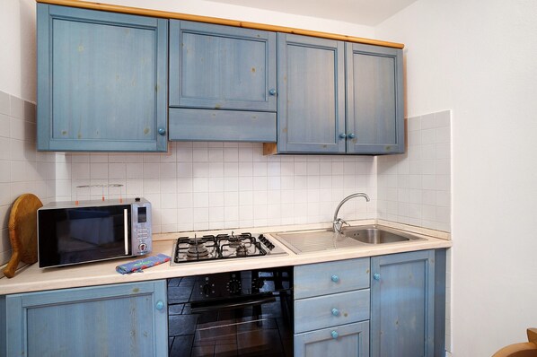 A kitchen with blue cabinets, a microwave, a gas stove, and a sink.