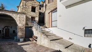 Un edificio de piedra con una escalera que lleva a un balcón, una banca y una pequeña mesa.