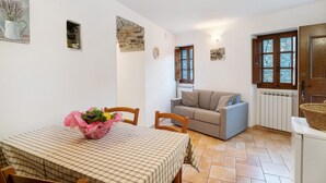 Un comedor con una mesa preparada para dos personas, un sofá y una ventana pequeña con arco de piedra.