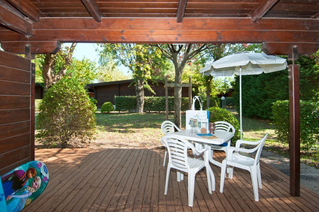 An outdoor wooden deck with a table and chairs, surrounded by greenery and trees.