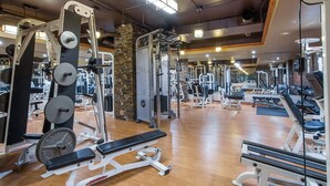 A gym with various exercise equipment, wooden flooring, and a stone pillar.
