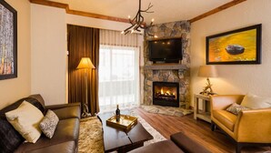 A cozy living room with a stone fireplace, leather sofas, a flat-screen TV, and a chandelier.
