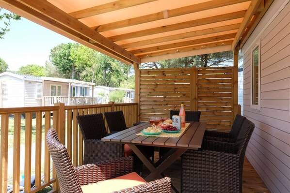 Un porche techado con muebles de mimbre y una mesa dispuesta para una comida, con vista a una zona residencial.