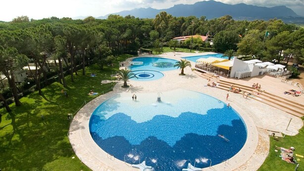 Une grande piscine circulaire, entourée de plusieurs petites piscines, d’une pelouse et d’arbres.