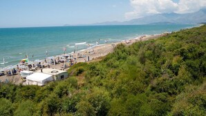 Une plage avec des tentes et des chaises de plage, un ciel dégagé et des montagnes en arrière-plan.