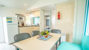 A compact kitchen with a microwave, refrigerator, and a small dining area with a table and chairs. - Cisano San Vito Mobilehome Happy Premium with panoramic view for 7 people (Cisano di Bardolino)