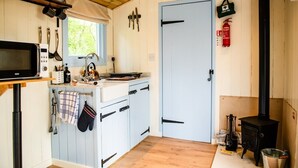 Une cuisine compacte équipée d’un four à micro-ondes, d’une cuisinière et de divers ustensiles. Une trousse de premiers secours et un extincteur sont fixés au mur.