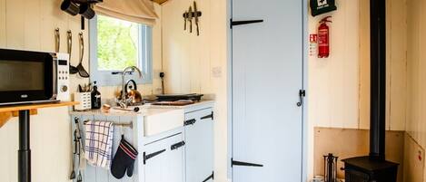 A compact kitchen with a microwave, stove, and various utensils. A first aid kit and fire extinguisher are mounted on the wall.